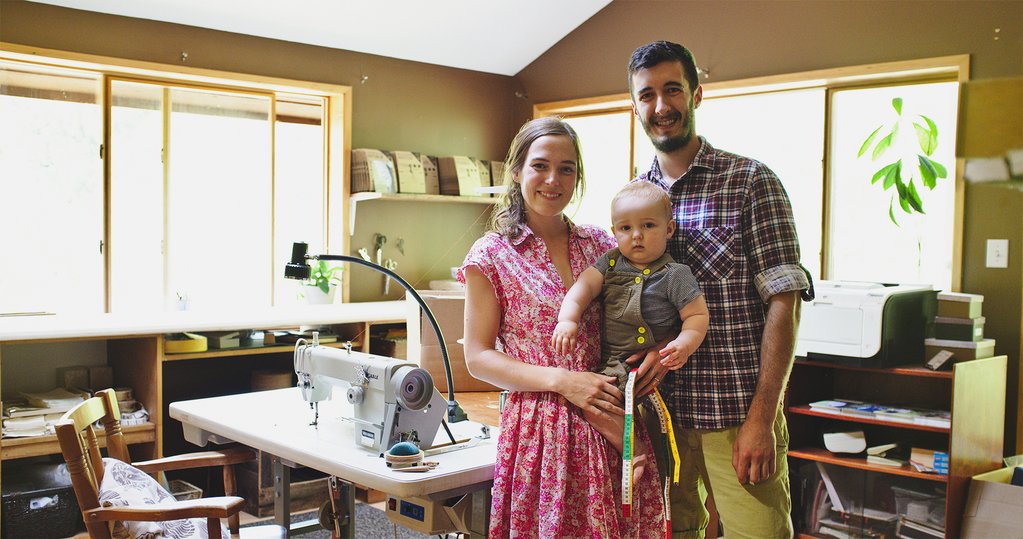Portrait of Matt and Morgan Meredith and their baby boy Noah, standing in their Thread Theory workshop in Victoria BC. 